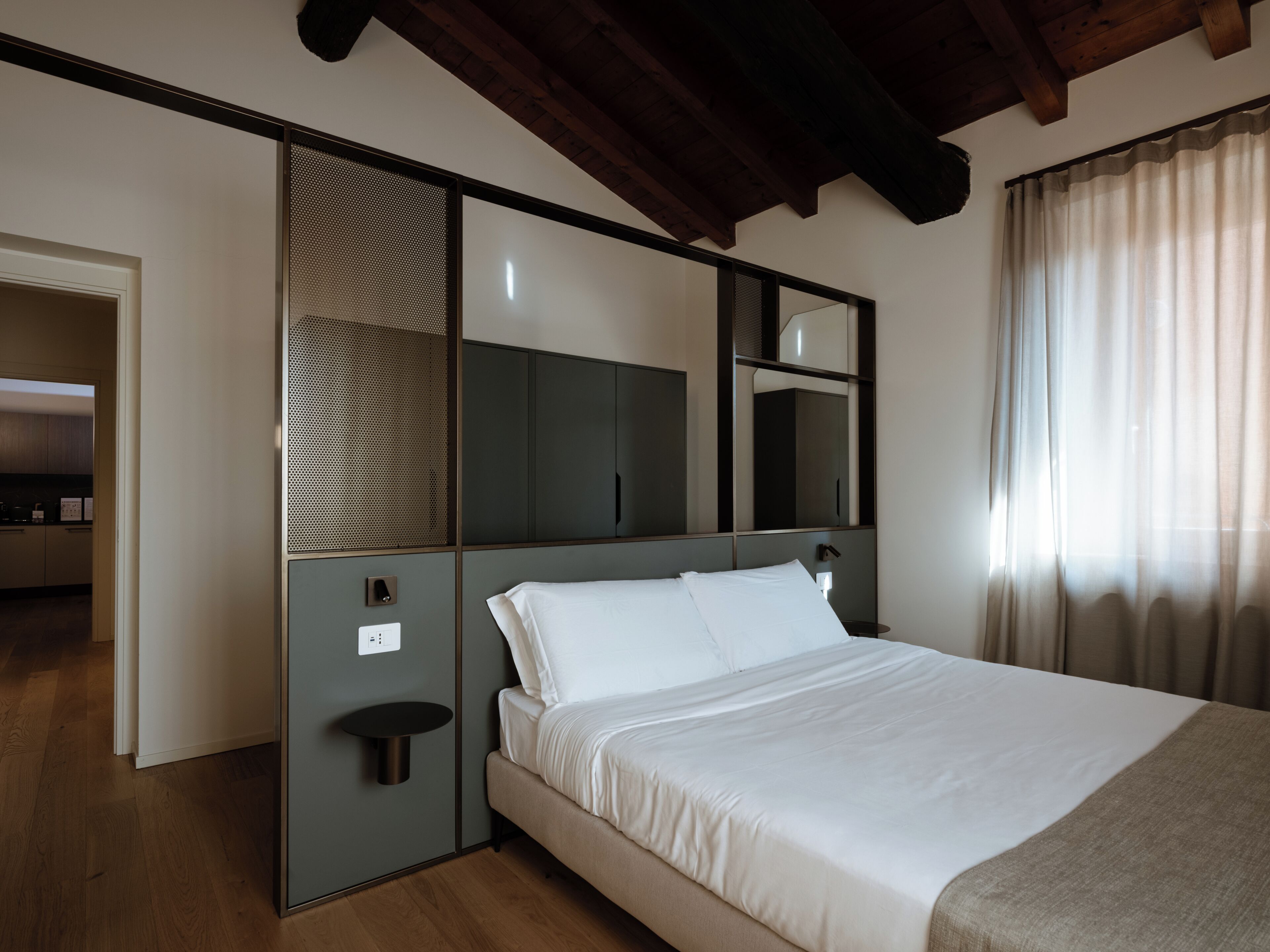 Habitación de hotel con cama, un espejo grande, un armario y una mesita.