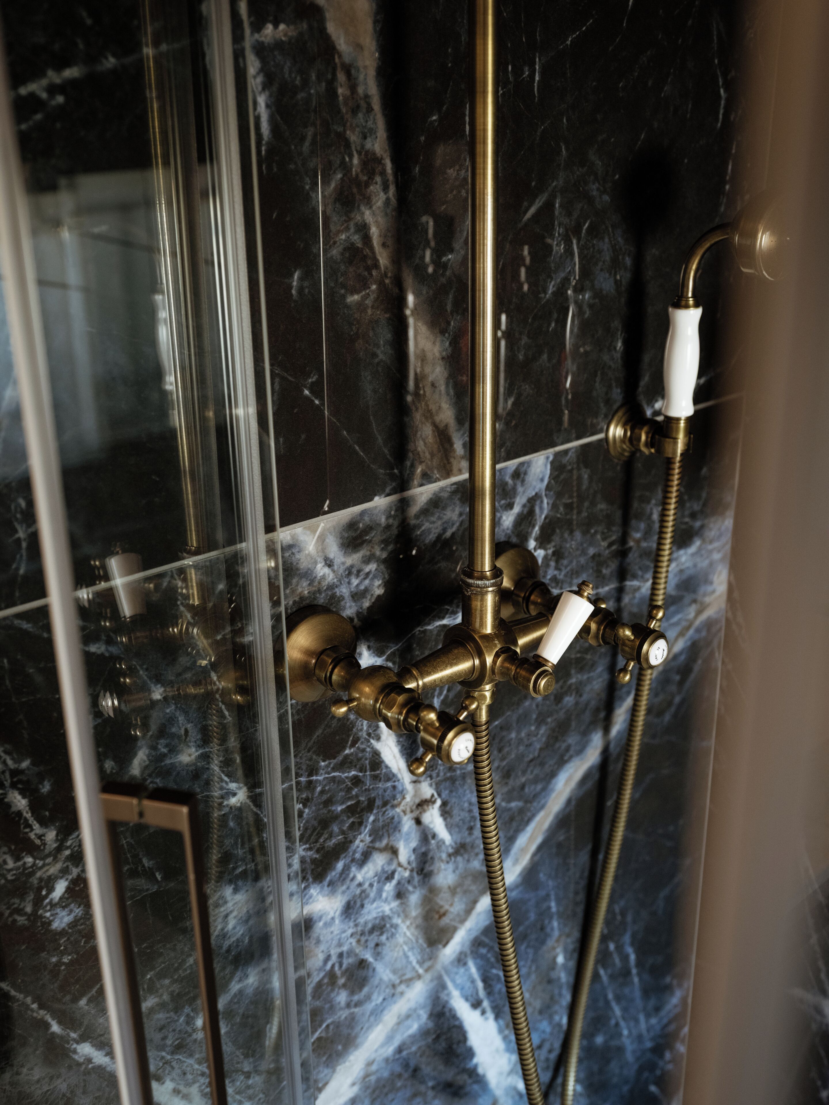 Une douche dotée d’un robinet et d’un tuyau en laiton, installée devant un mur de marbre.