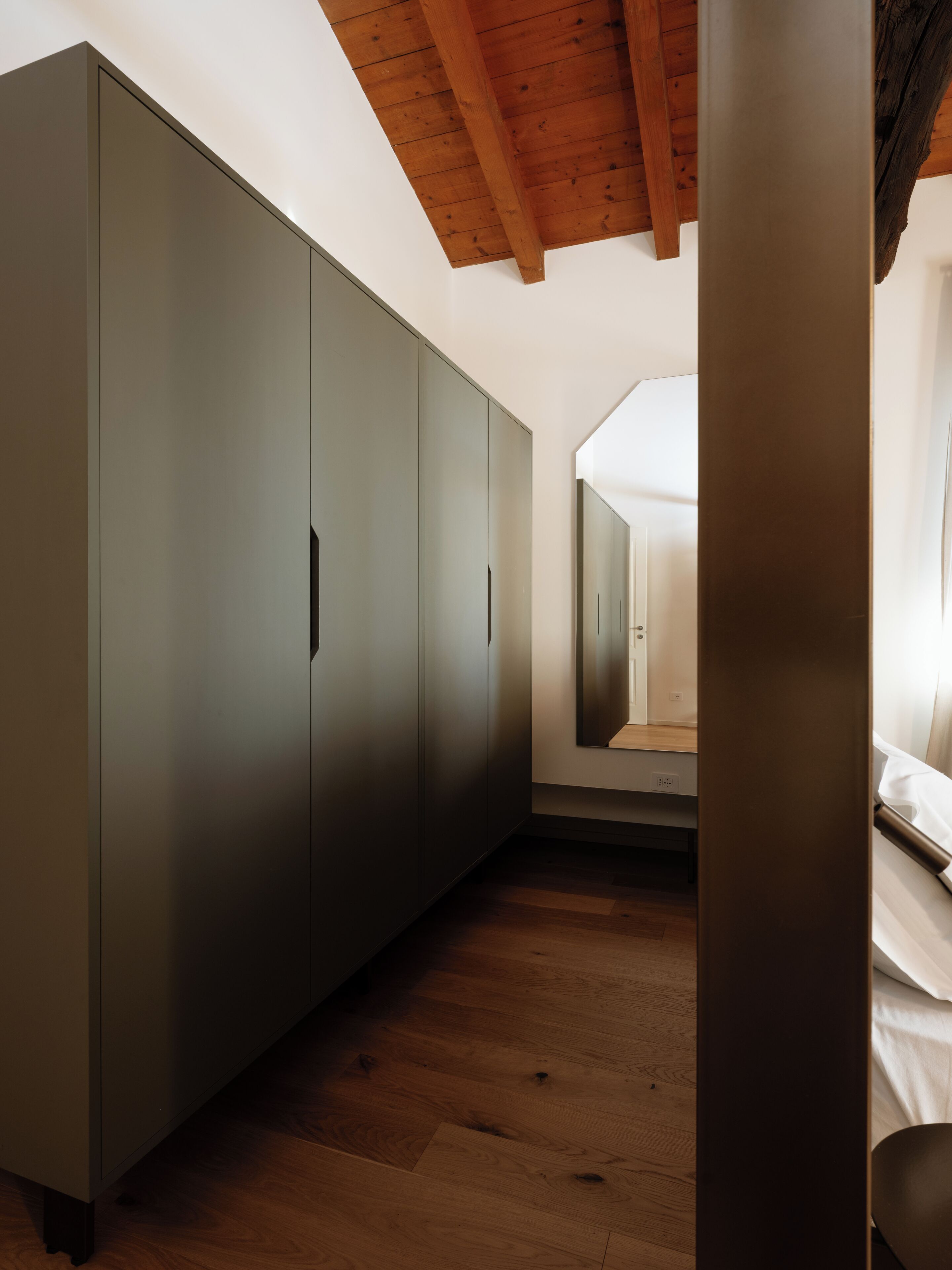 A room with a large wardrobe, a wooden floor, and a ceiling with exposed beams.