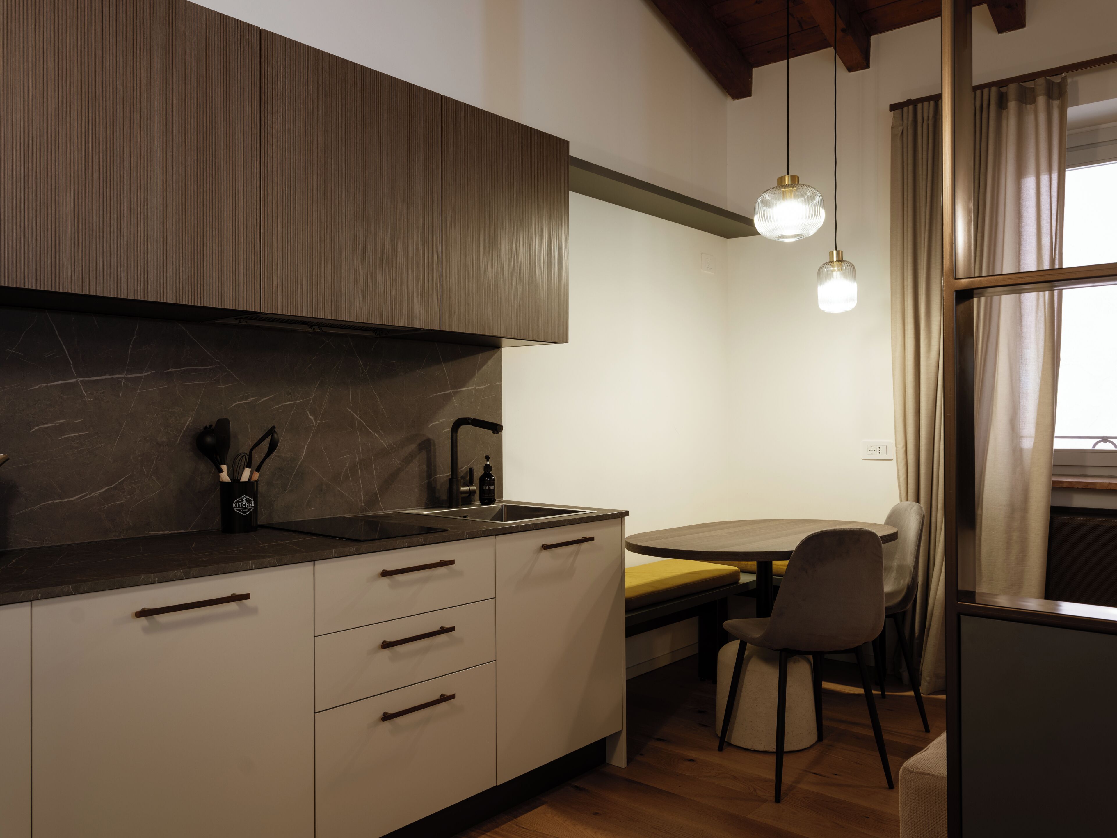 Una cucina moderna con un piano di lavoro scuro, mobili bianchi e un piano cottura integrato. È presente una zona pranzo con un tavolo e sedie.