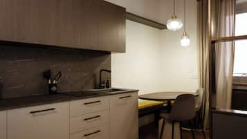 Una cucina moderna con un piano di lavoro scuro, mobili bianchi e un piano cottura integrato. È presente una zona pranzo con un tavolo e sedie.