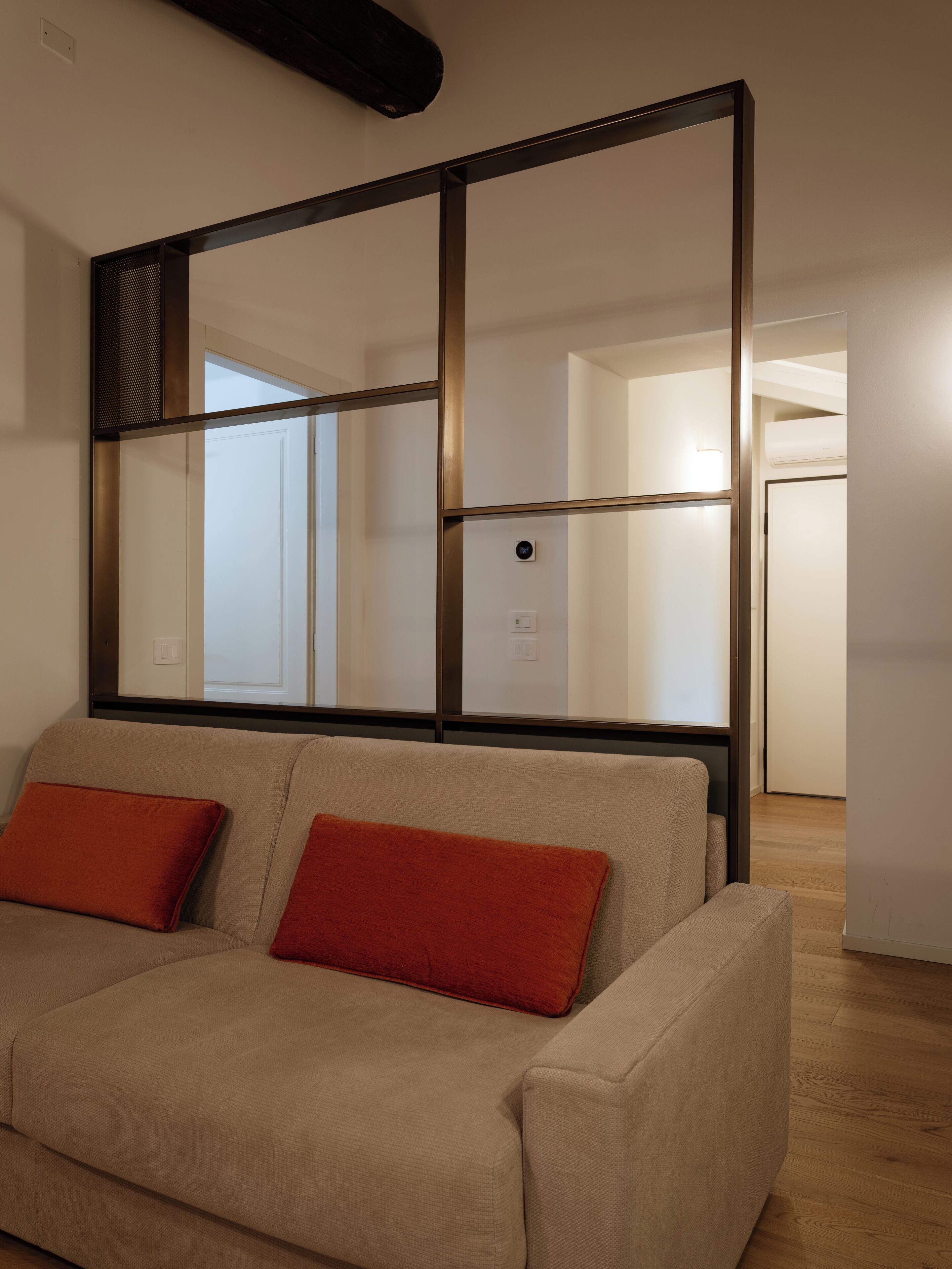 A neutral-toned sofa with two red cushions, a large mirror with a black frame, and a visible door leading to another room.