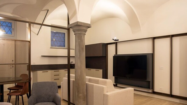 A modern hotel room with a large bed, a seating area with a sofa and chairs, a television, and a kitchen area. - Ca Moroni Collection (Bergamo)