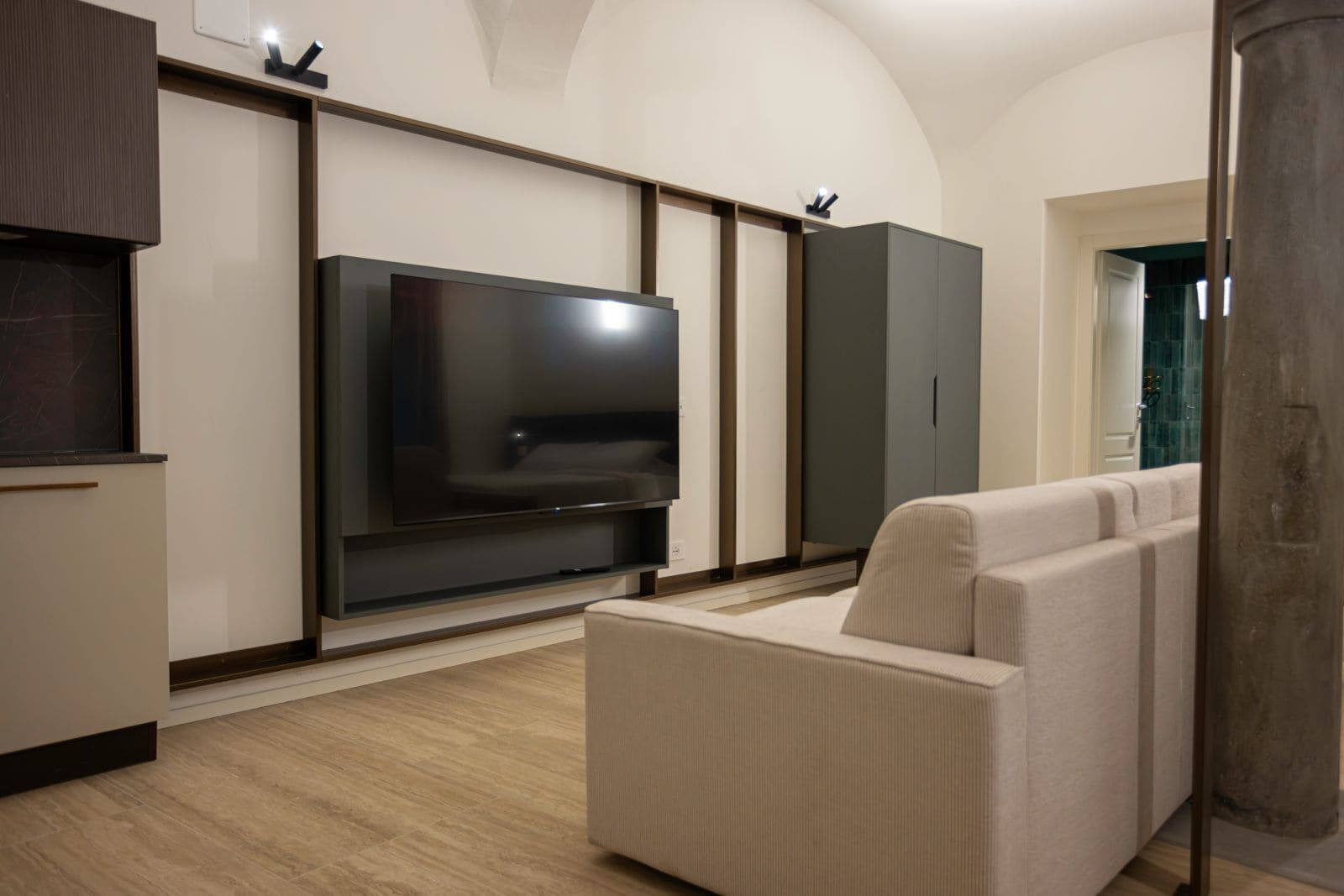 A modern living room with a large flat-screen TV, a beige sofa, and built-in cabinets.