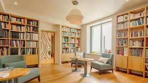 A spacious library with multiple bookshelves, comfortable seating, and a large window providing natural light.
