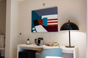 A hotel room with a desk, a coffee maker, a lamp, and a painting on the wall. - DOMAINE DE LA PEYRINE (Carignan-de-Bordeaux)
