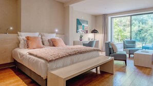 A modern bedroom with a large bed, a desk, and a seating area by a large window.