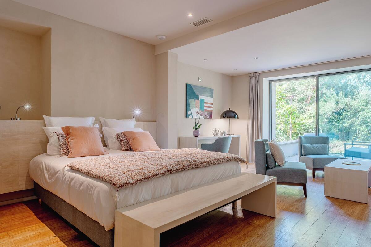 A modern bedroom with a large bed, a desk, and a seating area by a large window.