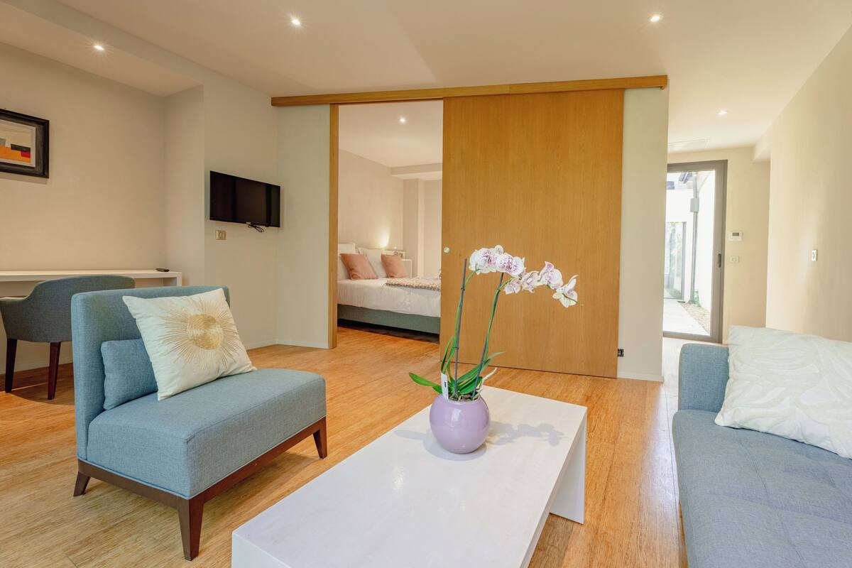A modern living room with a sofa, a coffee table with a vase of flowers, and a television mounted on the wall.