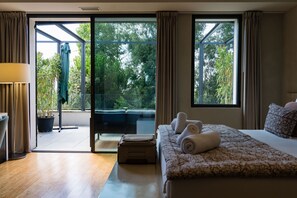 Un dormitorio con una cama grande, un sofá, una mesa y un ventanal corredero que da a un espacio exterior con plantas.