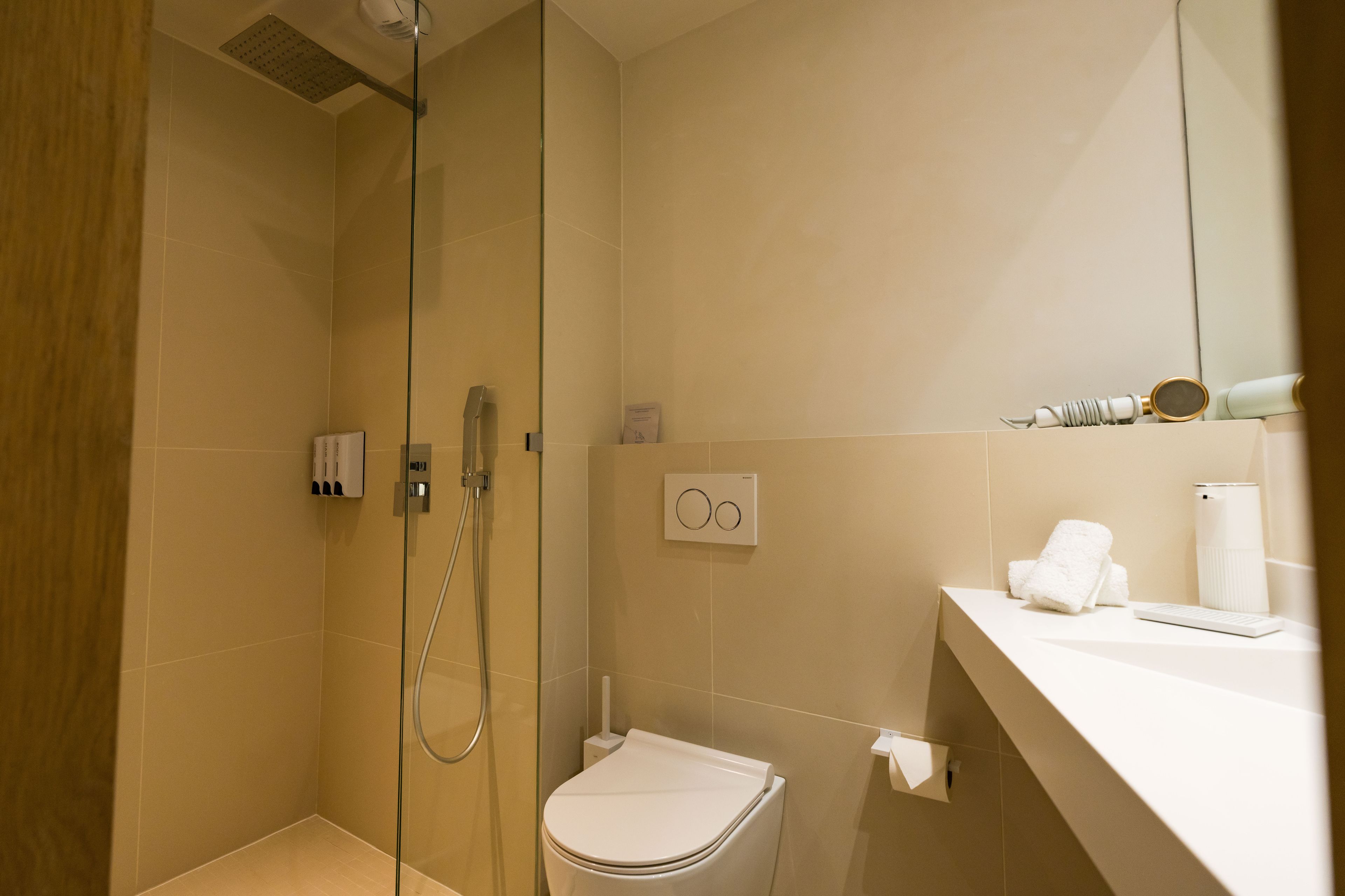 Un baño moderno con ducha de vidrio, inodoro y zona de lavamanos con toalla y secador de pelo.