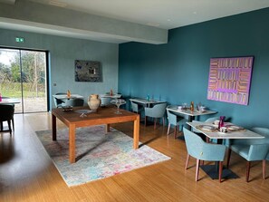 A modern dining area with a wooden table and chairs, a colorful rug, and a view through large glass doors. - DOMAINE DE LA PEYRINE (Carignan-de-Bordeaux)