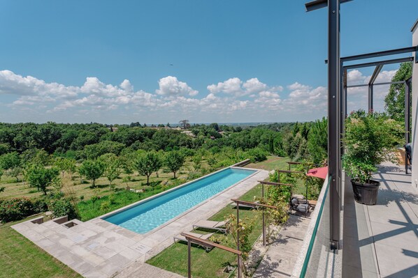 A swimming pool with a clear view of the surrounding landscape, including trees and a distant building. - DOMAINE DE LA PEYRINE (Carignan-de-Bordeaux)