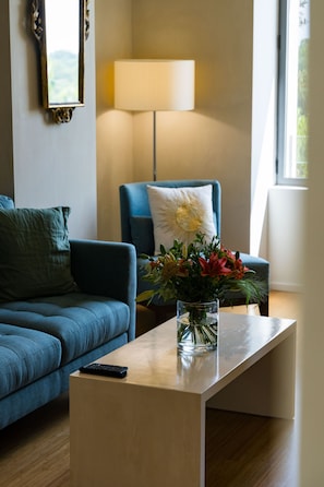 A living room with a blue sofa, a coffee table with a vase of flowers, a lamp, and a window. - DOMAINE DE LA PEYRINE (Carignan-de-Bordeaux)