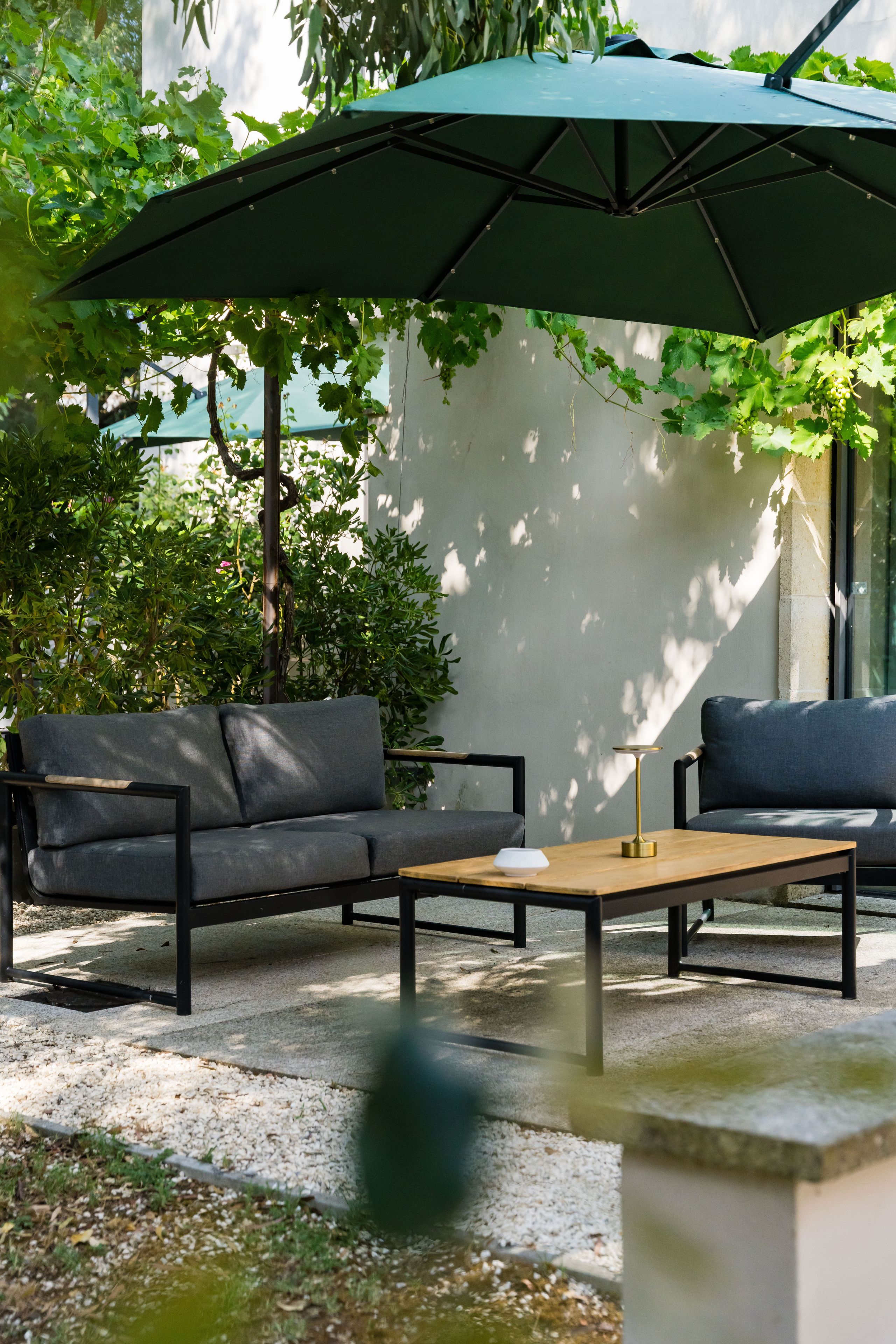 An outdoor seating area with a table and two sofas under a green umbrella.