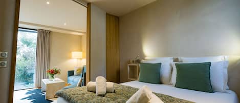Una habitación de hotel moderna con una cama grande, una zona de estar con una silla y una mesa, y vistas a través de un ventanal.
