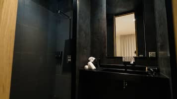 Ein modernes Badezimmer mit einer dunkel gefliesten Wand, einem großen Spiegel, einem schwarzen Waschbecken und einem Handtuch auf der Ablagefläche.