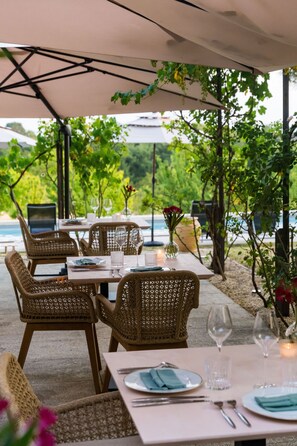 An outdoor dining area with wicker chairs and tables, set under a canopy, overlooking a body of water. - DOMAINE DE LA PEYRINE (Carignan-de-Bordeaux)