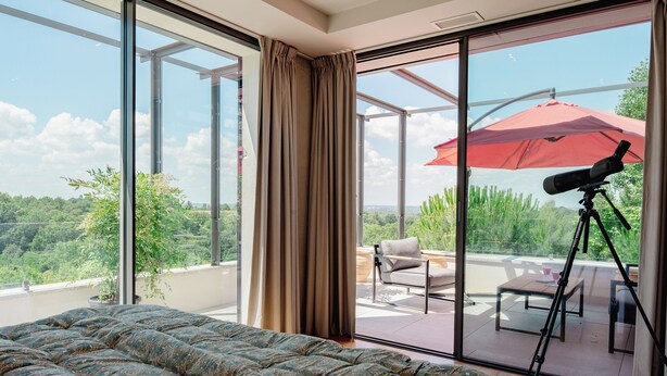 A bedroom with a large bed, sliding glass doors to an outdoor patio, and a telescope on a tripod.