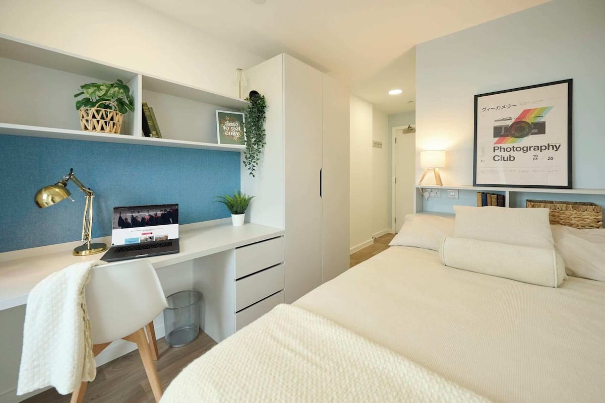 Une chambre à coucher moderne avec un bureau, un lit et une affiche encadrée au mur.