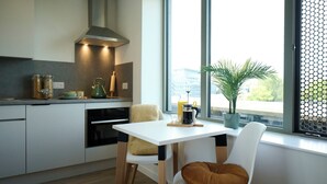 A modern kitchen with a white table, two chairs, a coffee maker, and a view of the city through a large window.