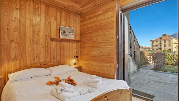 Dormitorio con paneles de madera, una cama, una mesita de noche, una fotografía enmarcada y vista a un patio.