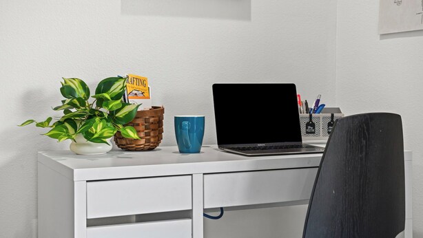 A white desk with a laptop, a blue mug, a plant, and a basket. - Old Town Condo Near CSU Pool, Sauna, Gym & Bikes (Fort Collins)