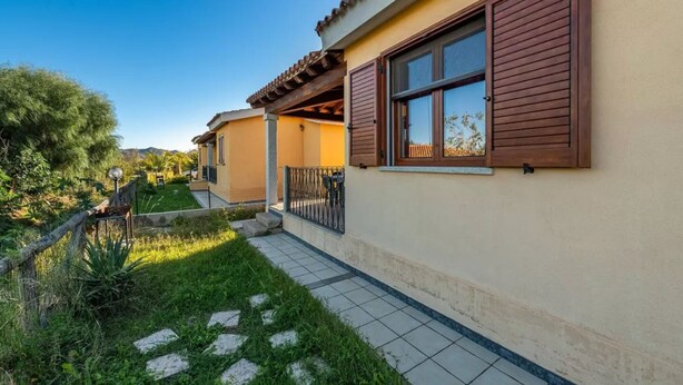 En bostadsbyggnad med en uteplats med kakelplattor, en täckt sittplats utomhus och en trädgård med stenplattor som man kan gå på.