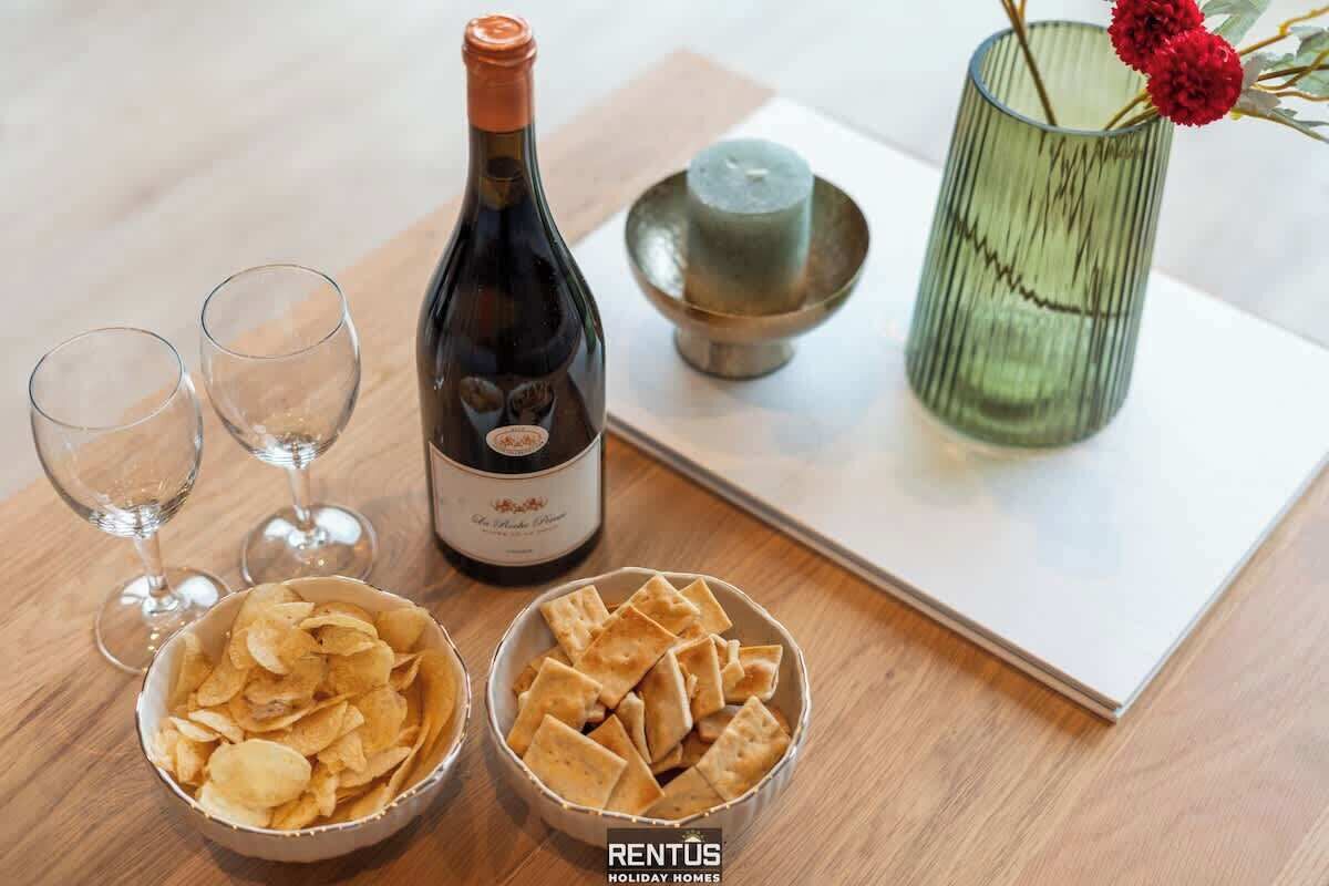 A table with a bottle of wine, two glasses, bowls of chips, and a candle in a glass holder.