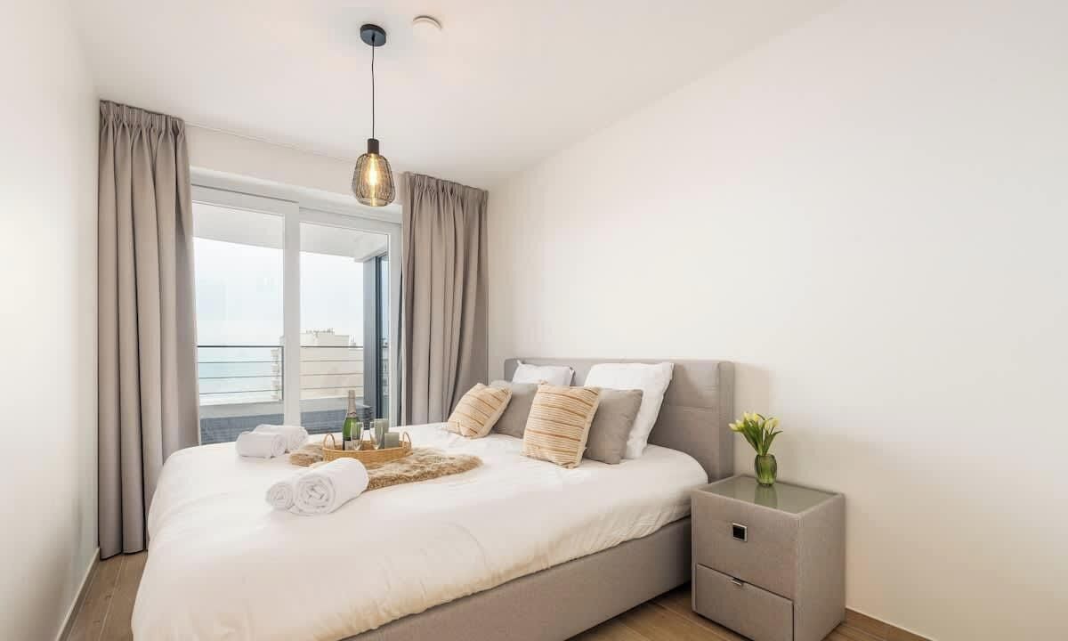 Een moderne slaapkamer met een groot bed, een nachtkastje en uitzicht op de stad door het raam.