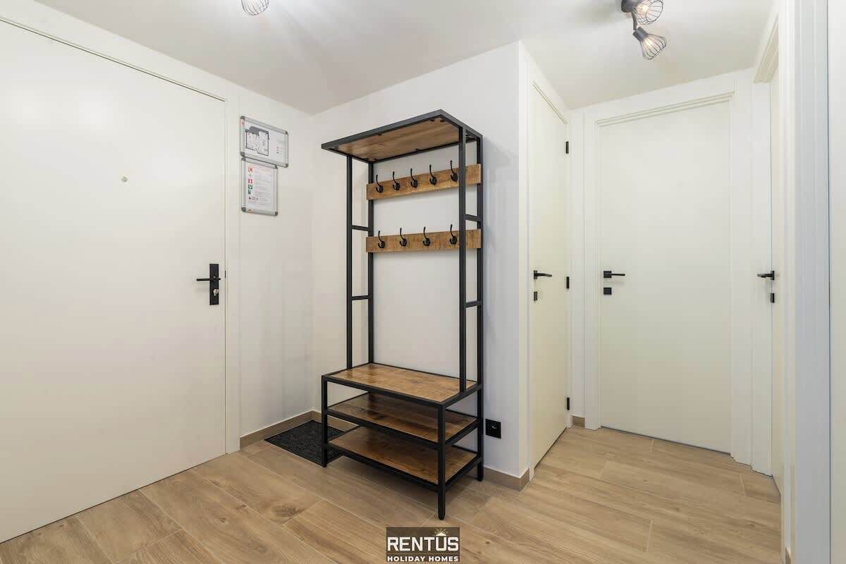 A hallway with a wooden and metal rack with hooks, white doors, and a light fixture.