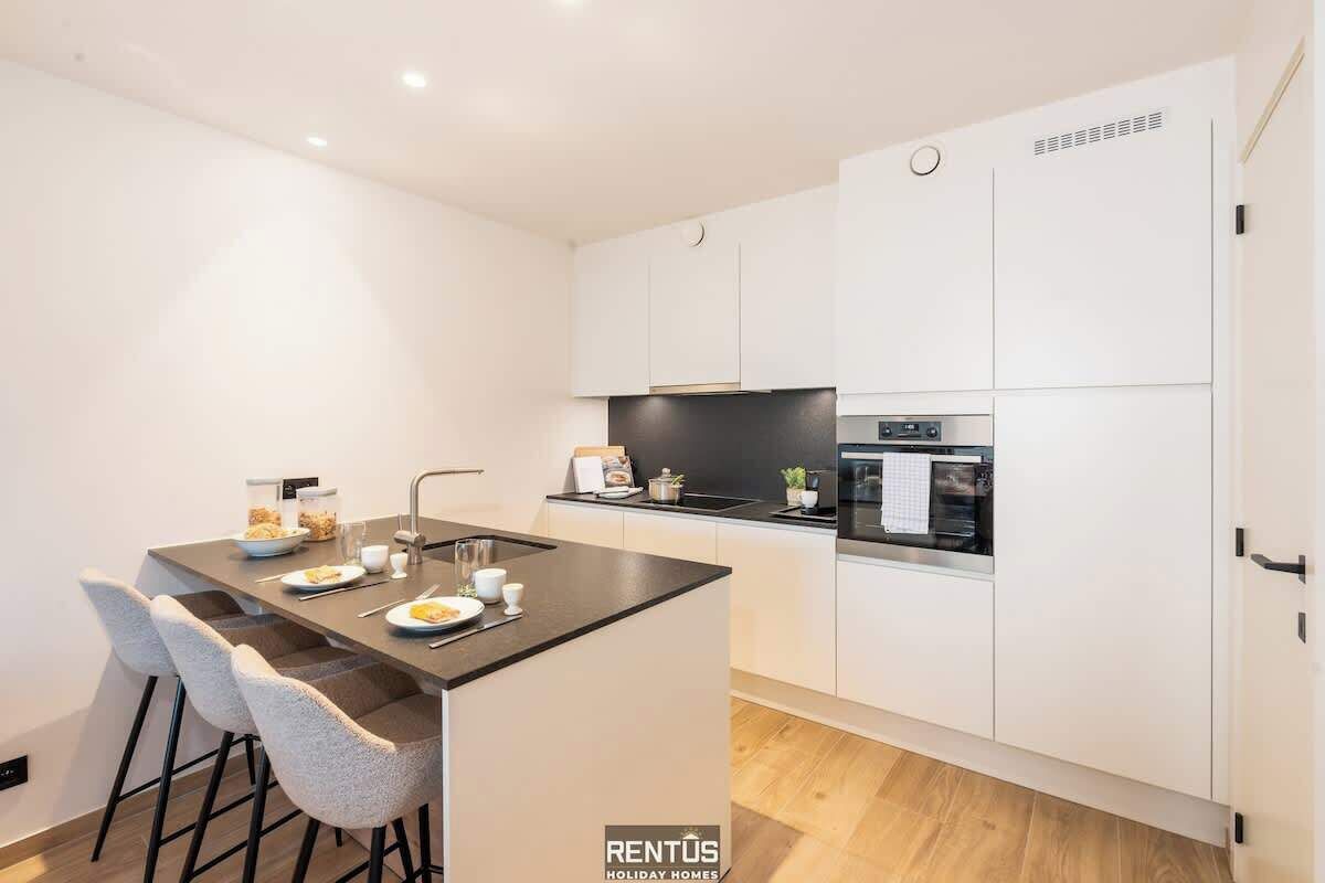 A modern kitchen with white cabinets, a black countertop island, and a built-in oven.