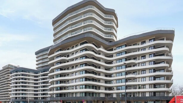 En modern, flervåningsbyggnad med en unik, böljande arkitektonisk design, utrustad med balkonger och stora fönster.