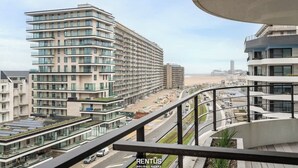 En hög byggnad med flera balkonger, en modern arkitektonisk design och utsikt över ett kustnära område med en väg och andra byggnader.