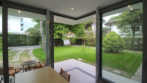 A modern interior with a large glass door leading to a well-maintained garden. - Modern villa 200mt from the beach (Lignano Sabbiadoro)