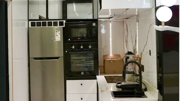 A compact kitchen with a refrigerator, oven, microwave, and a coffee machine. - Rahat luxury apartment (Lagos)