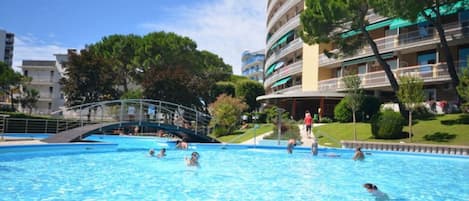 A swimming pool with people in the water, surrounded by buildings and trees.
