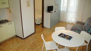 Un espacio habitable compacto con kitchenette, una zona de comedor con mesa y sillas, un sofá y un televisor.