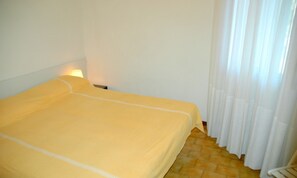 A single bed with a yellow bedspread in a room with white walls and a tiled floor. - Apartment 50mt from the beach (Lignano Sabbiadoro)