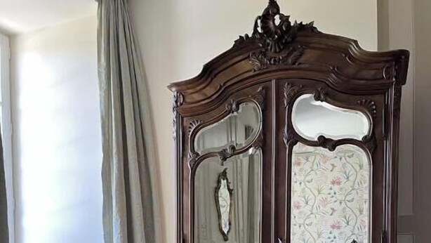 A room with a wooden chair and a large mirror cabinet.
