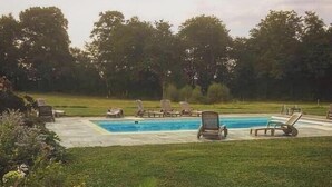 A swimming pool with lounge chairs, surrounded by grass and trees.