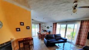 A living room with a fireplace, a sofa, a dining table with chairs, and a ceiling fan.