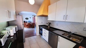A modern kitchen with white cabinets, a black countertop, and a dining area in the background.