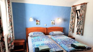 A double bed with patterned bedding, a nightstand, a wall-mounted light, and a window with curtains.