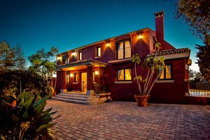 A two-story house with a brick facade, a balcony, and a well-lit entrance. - Villa Sunsets - charming villa in residential area in Elviria (Marbella)