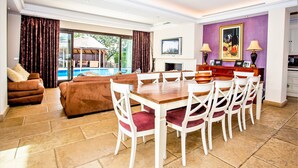 Un'ampia zona giorno con un grande tavolo da pranzo, comodi posti a sedere e vista su una piscina.