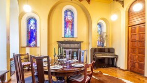 Une salle à manger avec une table ronde, des chaises, des vitraux, un piano et un tapis en peau de vache.