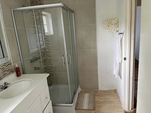 A bathroom with a glass-enclosed shower, a white sink, and a tiled shower area.