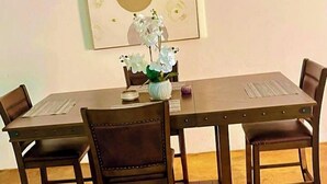 Un'area pranzo con un tavolo rettangolare e quattro sedie, un vaso con fiori bianchi e un'opera d'arte incorniciata sopra il tavolo.