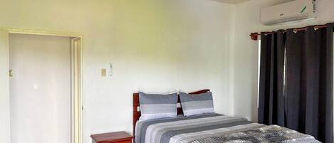 A bedroom with a bed, a nightstand, a ceiling fan, an air conditioner, and a door.
